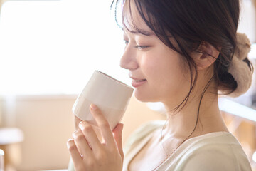 カップを手に持ち飲み物を飲む若い女性。