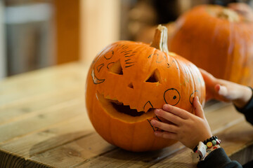 Kreativ geschnitzter Halloween-Kürbis auf Holztisch mit Kinderhand beim Dekorieren