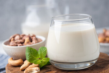 Cashew milk in a glass on wooden board background, closeup view. Healthy alternative dairy free milk choice