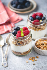 Greek yogurt parfait with granola and fresh berries in a jar on grey background. Healthy vegetarian snack or breakfast meal