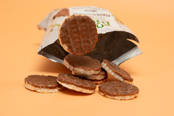 Open package with chocolate rice wafers on an orange background. Wafers with chocolate chips are scattered on the table.