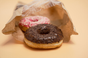 A chocolate and pink donut is sitting in a brown paper bag. The bag is on a table