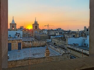 Obraz premium Sunrise over the rooftops and bell towers in Valletta, Malta, casting a warm glow over the historic architecture.