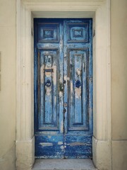 Weathered blue wooden door with peeling paint, set in a historic stone frame in Valletta, Malta.