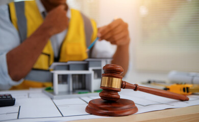 Judge gavel on building blueprint plans with a yellow safety helmet in the background. law that deals with matters relating to building construction, engineering. Construction law concept.