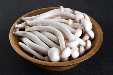 White Shimeji mushroom in wooden bowl on a dark background.