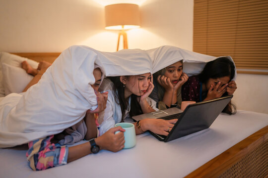 A group of friends is enjoying a fun movie night together, all snuggled up under warm blankets - Powered by Adobe