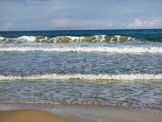 Nahe Aufnahme von Wellen, die sich über den Sandstrand bewegen. Das Meer hinter den Wellen liegt im Schatten, was einen dramatischen Kontrast zum helleren Vordergrund schafft.