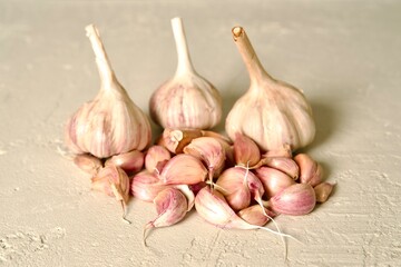 Fresh garlic bulbs with stems intact, arranged on a light, textured surface, showcasing their natural rustic appearance.
