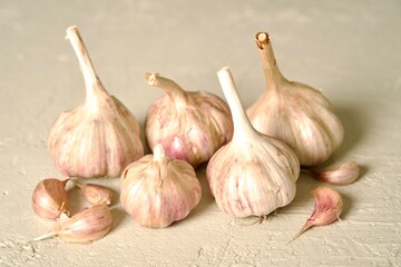Fresh garlic bulbs with stems intact, arranged on a light, textured surface, showcasing their natural rustic appearance.