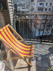 A vibrant, bright wooden sun lounger stands on a cozy balcony, catching natural light. Its warm wood tones create a cheerful contrast against the surroundings, inviting relaxation and a connection wit