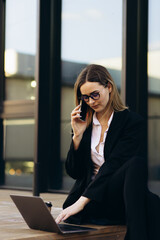 Business woman working on laptop outside the building and drinking coffee