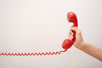 close up of Hand holding red telephone receiver with coiled cord extended against light grey...