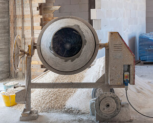 concrete mixer installed on the construction site next to a pile of sand and gravel.
