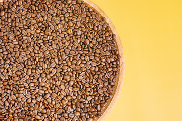 Roasted coffee beans on a wooden tray on a yellow background.