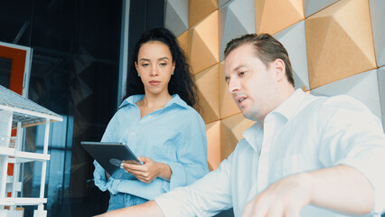 Portrait of project manager pointing at house model while discussion about building design. Caucasian cooperative architect engineer team brainstorming about building material. Teamwork. Manipulator.