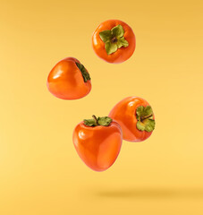 Fresh ripe Persimone fruit falling in the air isolated on yellow background, food levitation or zero gravity conception