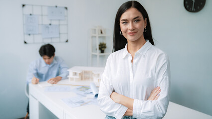 Fototapeta premium Closeup of female professional architect engineer cross arms with confident while skilled coworker focus on drawing blueprint at table with house model. Creative living and design concept. Immaculate.