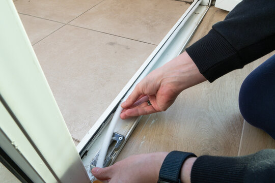 Preparing for the cold season. A man sticks a white foam rubber sealing tape on a door window indoors. Saving Energy Insulating Home Putting Draught Excluder Tape On Window