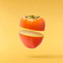 Fresh ripe Persimone fruit falling in the air isolated on yellow background, food levitation or zero gravity conception
