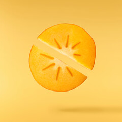 Fresh ripe Persimone fruit falling in the air isolated on yellow background, food levitation or zero gravity conception