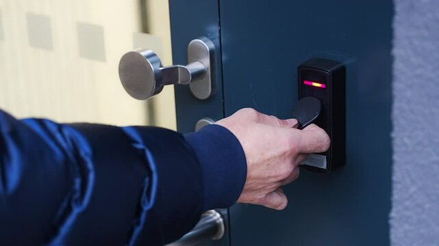 Close up view of person using a electric lock key fob to access a building via a reader of entry system mounted on a house wall