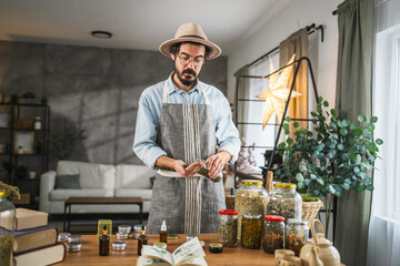 Adult young man herbalist pours herbs from a jar at workshop © Miljan Živković