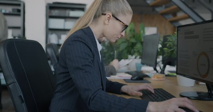 Young businesswoman in suit using personal computer working online sitting at desk in shared office. Business and coworking center concept.