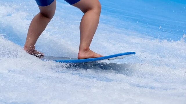 A man rides a surfboard on a wave simulator indoors. Young surfer during training on generated waves. Water sports and recreation.