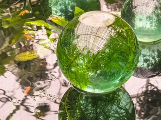 Glass sphere with an air pocket in a shallow artificial pool, with distorted reflections of greenery and gridwork ceiling, in a tropical garden conservatory. (Selective focus.) A modern gazing ball.