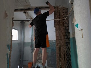 A man breaks plaster on the wall. Demolition work site. Interior work.