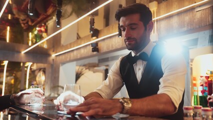 Focusing on smart bartender serving gin fizz or tonic at luxurious bar while engaging lively conversation with VIP customer at vibrant warm lighting atmosphere at lighting warm nightclub. Vinosity.