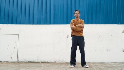 Hispanic man stretch arms and dance street dancing in front of wall. Motion shot of stylish dancer or choreographer in casual outfit practicing dancing in hip hop style. Outdoor sport 2024. Hiphop.