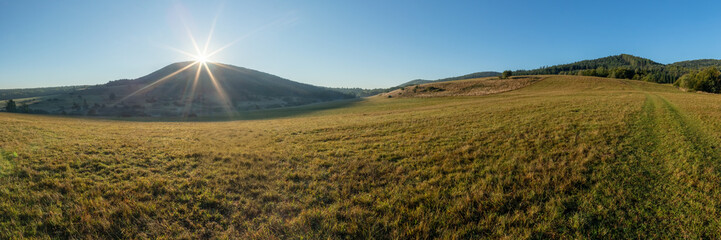 Landscape of Beskid Niski mountains. Pastures, meadows, and forested hills. Rays of the rising sun. Areas of a non-existent Lemko village. Rising Regietow Wyżny, Poland, Europe. HDR panorama.