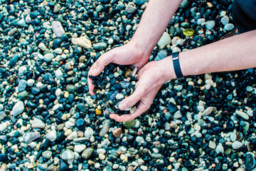 a man holds pebbles from the sea coast in his hands