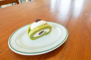 Delicious Matcha Green Tea Roll Cake and red beans on wooden table, Japanese Dessert Style With white vanilla cream inside.
