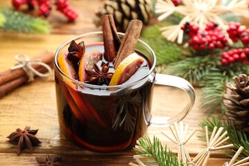 Tasty mulled wine with spices, orange slices and Christmas decor on wooden table, closeup