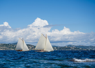 Historic sail yachts in the bay of St. Tropez sailing in blue water under a blue sky on a sunny day.