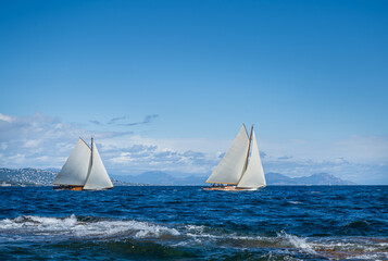 Historic sail yachts in the bay of St. Tropez sailing in blue water under a blue sky on a sunny day.