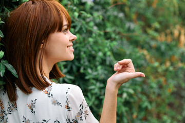 Woman standing gracefully with hand extended towards bush in a peaceful outdoor setting