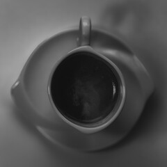 A dramatic black and white photograph of a coffee cup with a saucer, captured in low-key lighting. The deep shadows and subtle highlights emphasize the elegant curves and details of the cup, creating 
