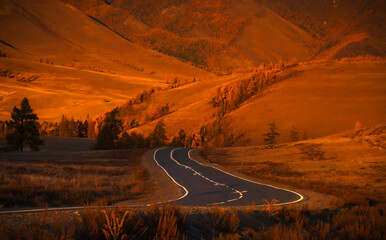 Curvy mountain road amidst vibrant autumn foliage during sunset, highlighting golden hues and tranquil scenery, ideal for travel and nature themes or adventure inspirations © Anton Gvozdikov