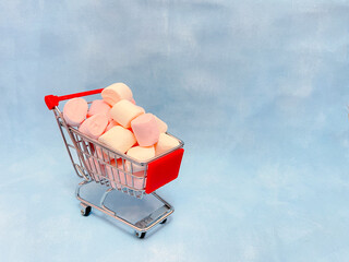 Miniature cart from a supermarket with marshmallows. Blue background