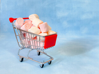 Miniature cart from a supermarket with marshmallows. Blue background