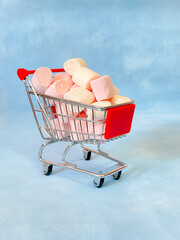 Miniature cart from a supermarket with marshmallows. Blue background