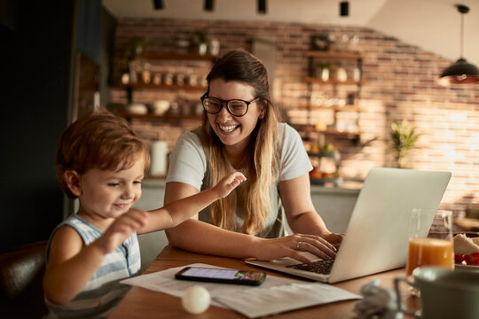 Mother working from home with young son by her side at kitchen table