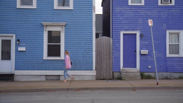 A blond Hair Girl in a Pink Shirt Passing Walking on the Street and Passes by two Blue Houses 4K 