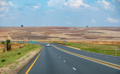 Highway in South African countryside. Asphalt road, fields and farmland background, blue cloudy sky