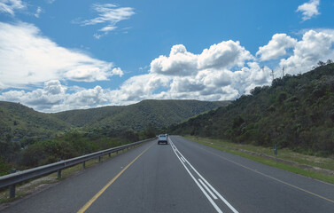 Highway in South African countryside. Asphalt road stretches ahead, green hills and blue sky with fluffy clouds