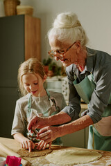 Elderly woman teaching young girl baking, both enjoying shared activity in cozy kitchen setting....